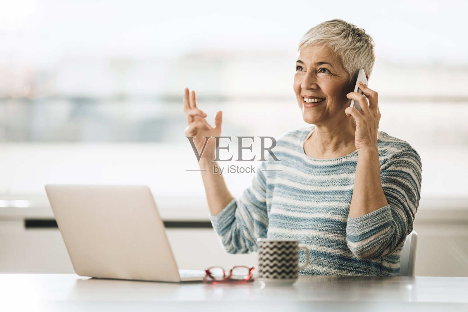 快乐成熟的女人在家里用笔记本电脑打电话。照片摄影图片