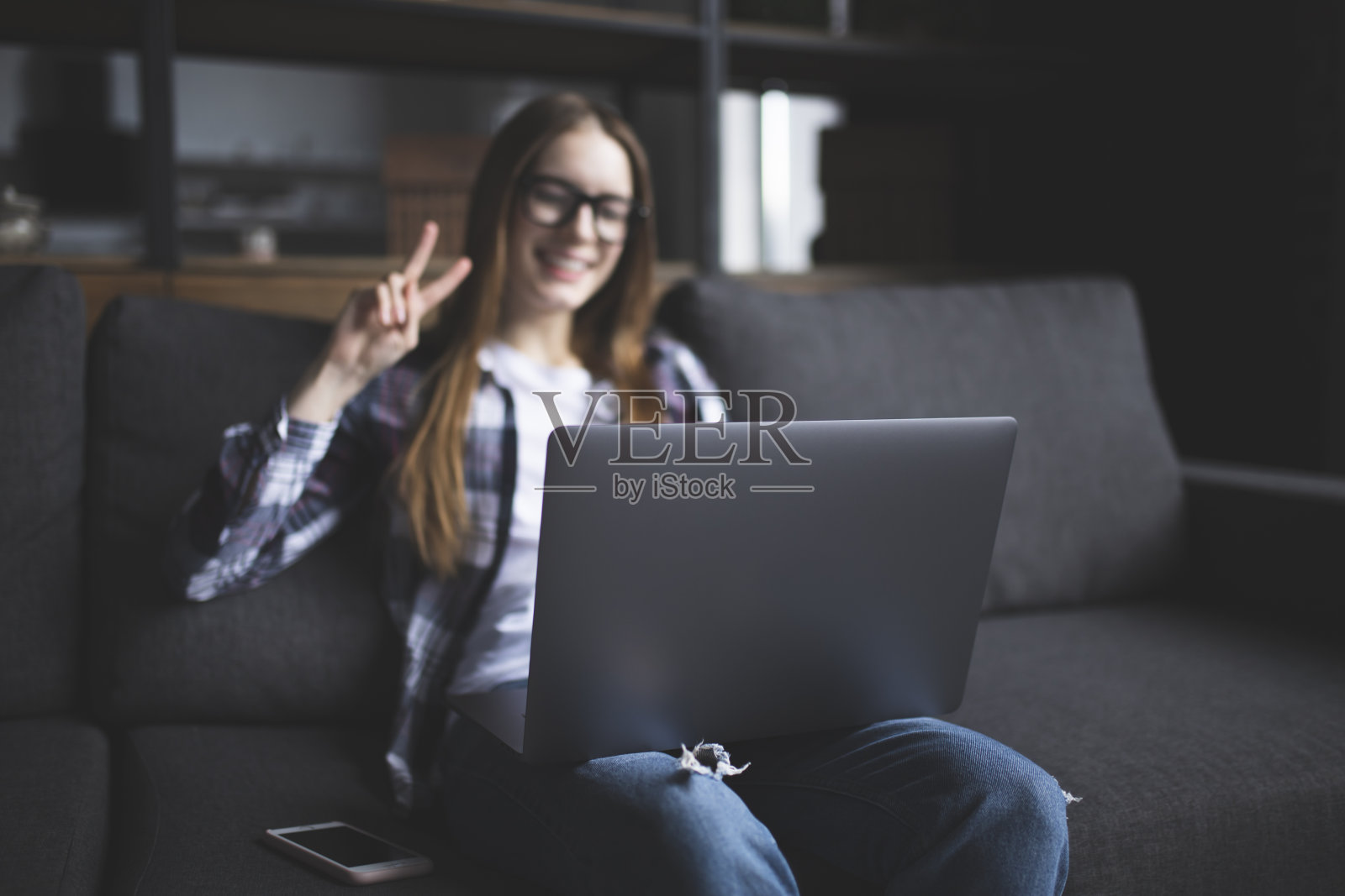 一个戴着眼镜的可爱女孩的肖像，在沙发上拿着笔记本电脑照片摄影图片