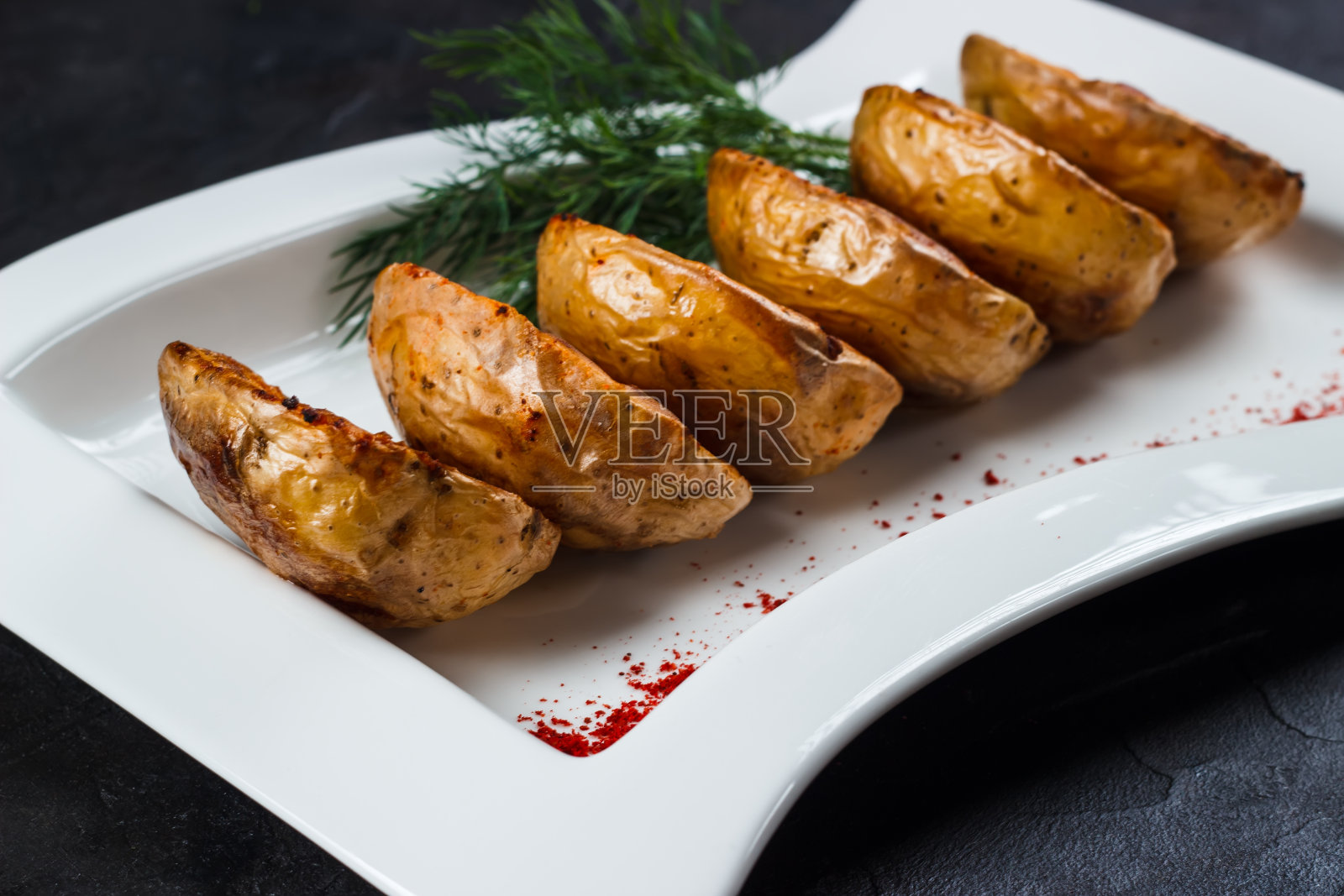 将烤土豆片放在用红辣椒和莳萝装饰的白色盘子上照片摄影图片