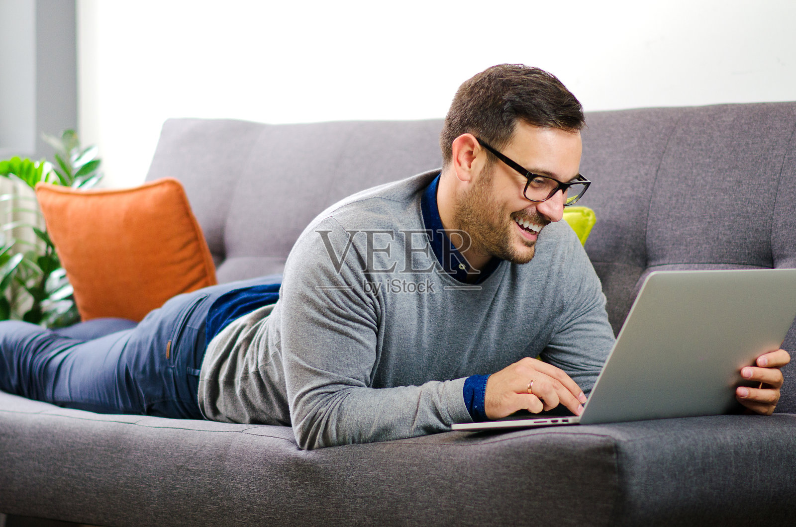轻松愉快的自由职业者在家用笔记本电脑工作，躺在沙发上微笑。照片摄影图片