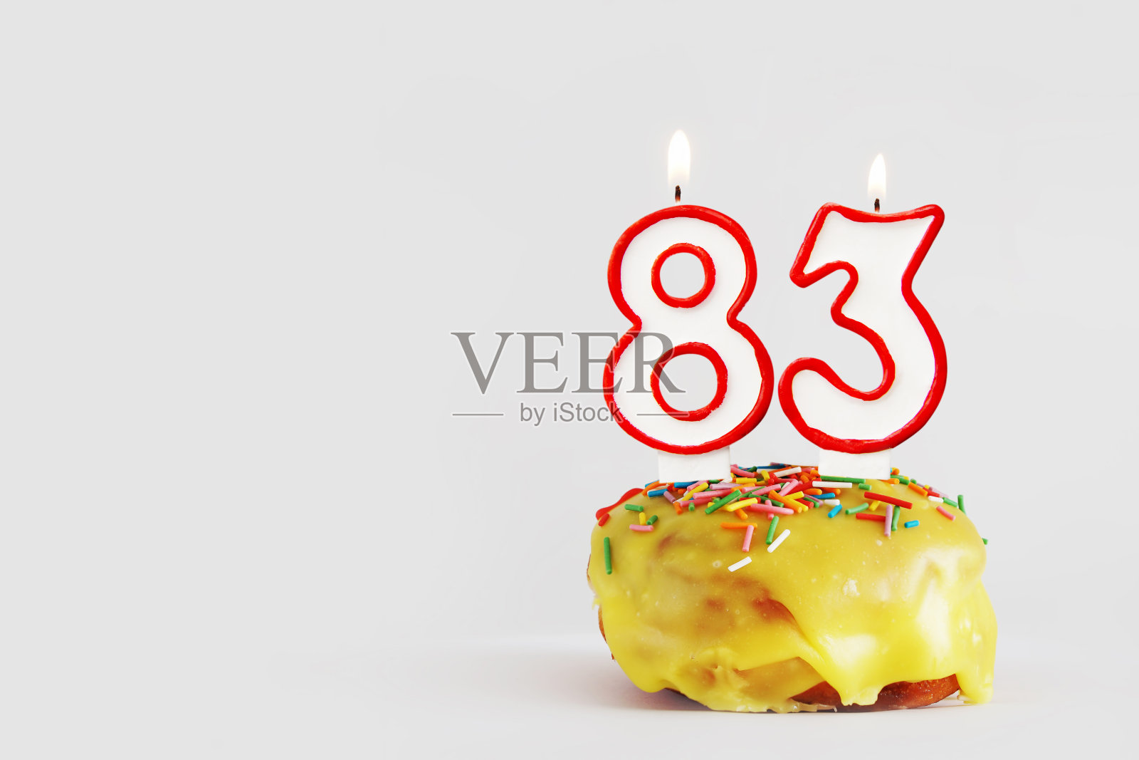 83周年纪念日。生日纸杯蛋糕与白色燃烧的蜡烛与红色边框形式的83数字。浅灰色背景与复制空间照片摄影图片