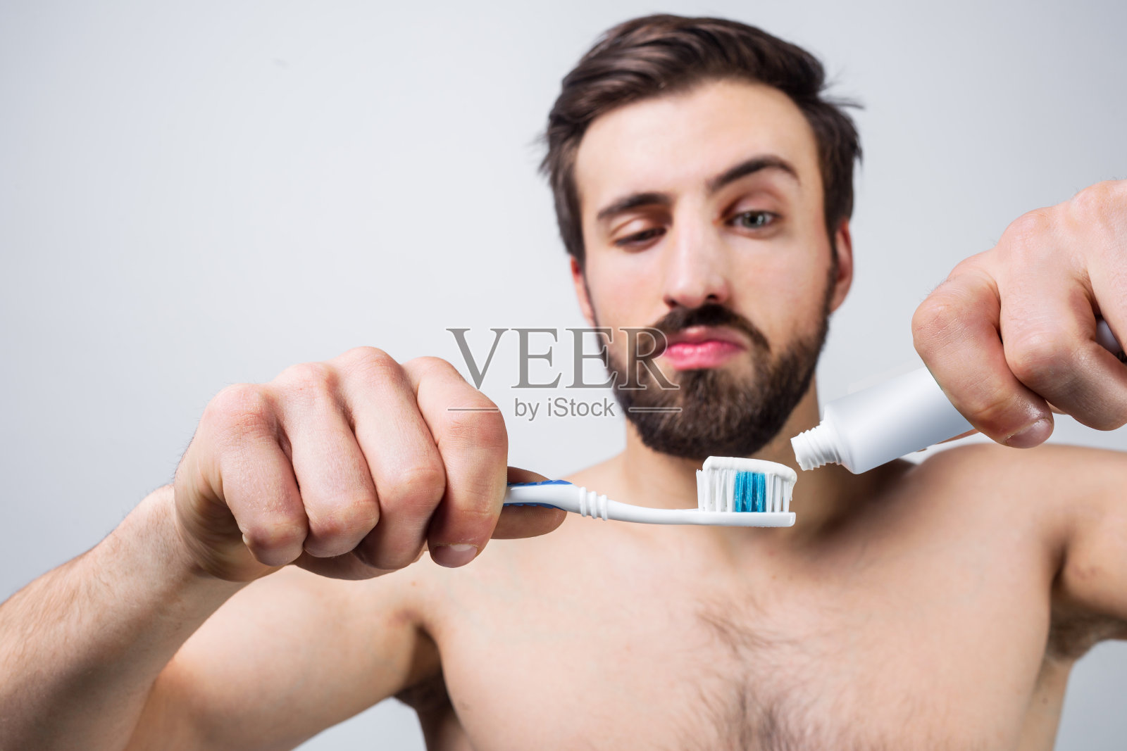 帅哥在往牙刷上涂牙膏。他每天早晚上厕所的时候都会重复这个动作。减少视图。在白色背景上隔离照片摄影图片
