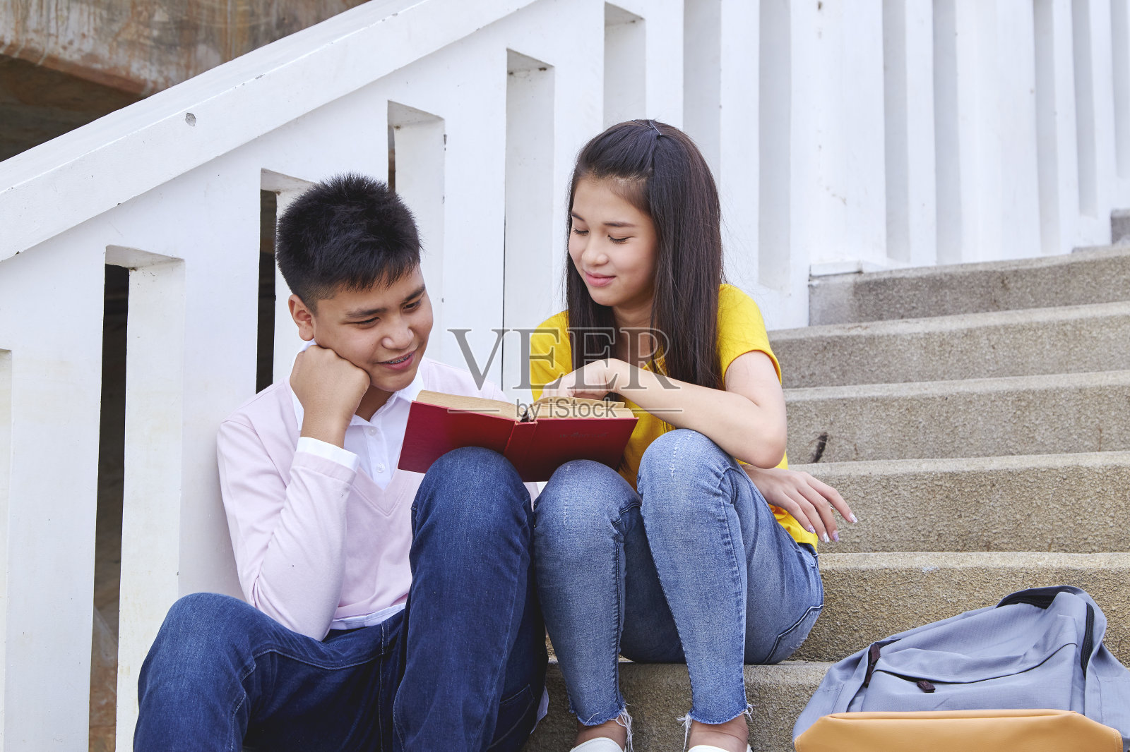 坐在楼梯上的亚洲学生。情侣们用迷人的微笑看书和笔记本电脑照片摄影图片