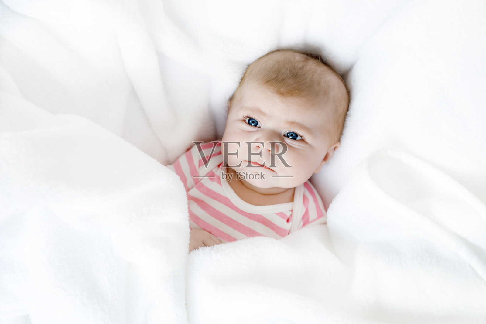可爱可爱的新生婴儿躺在白色的床上。刚出生的孩子，可爱的小女孩惊讶地看着镜头。家庭，新生活，童年，开始的概念。照片摄影图片