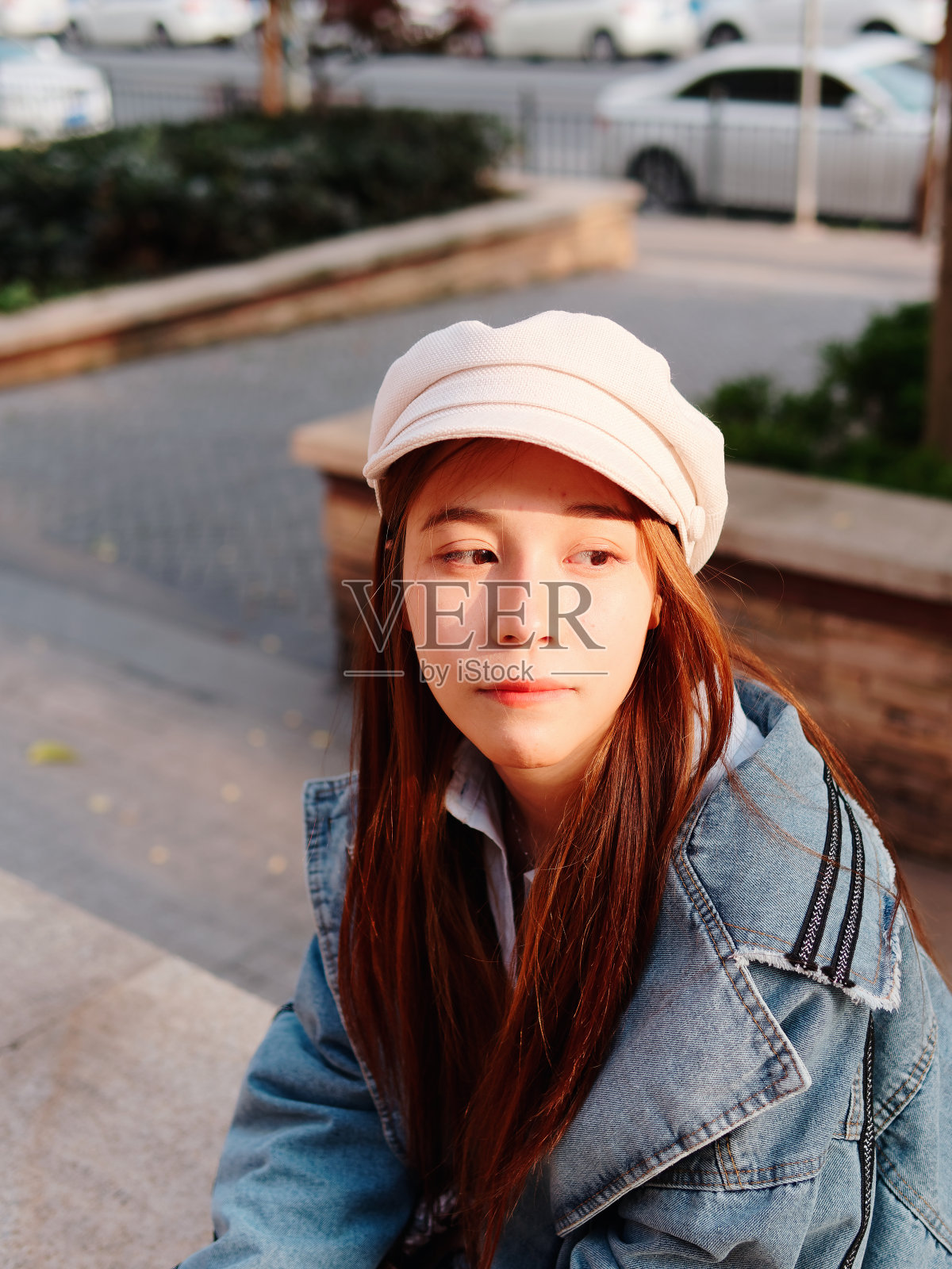 街道摄影一个可爱的中国年轻女人穿着牛仔裤和白色帽子，模糊的街道背景，女性肖像。照片摄影图片