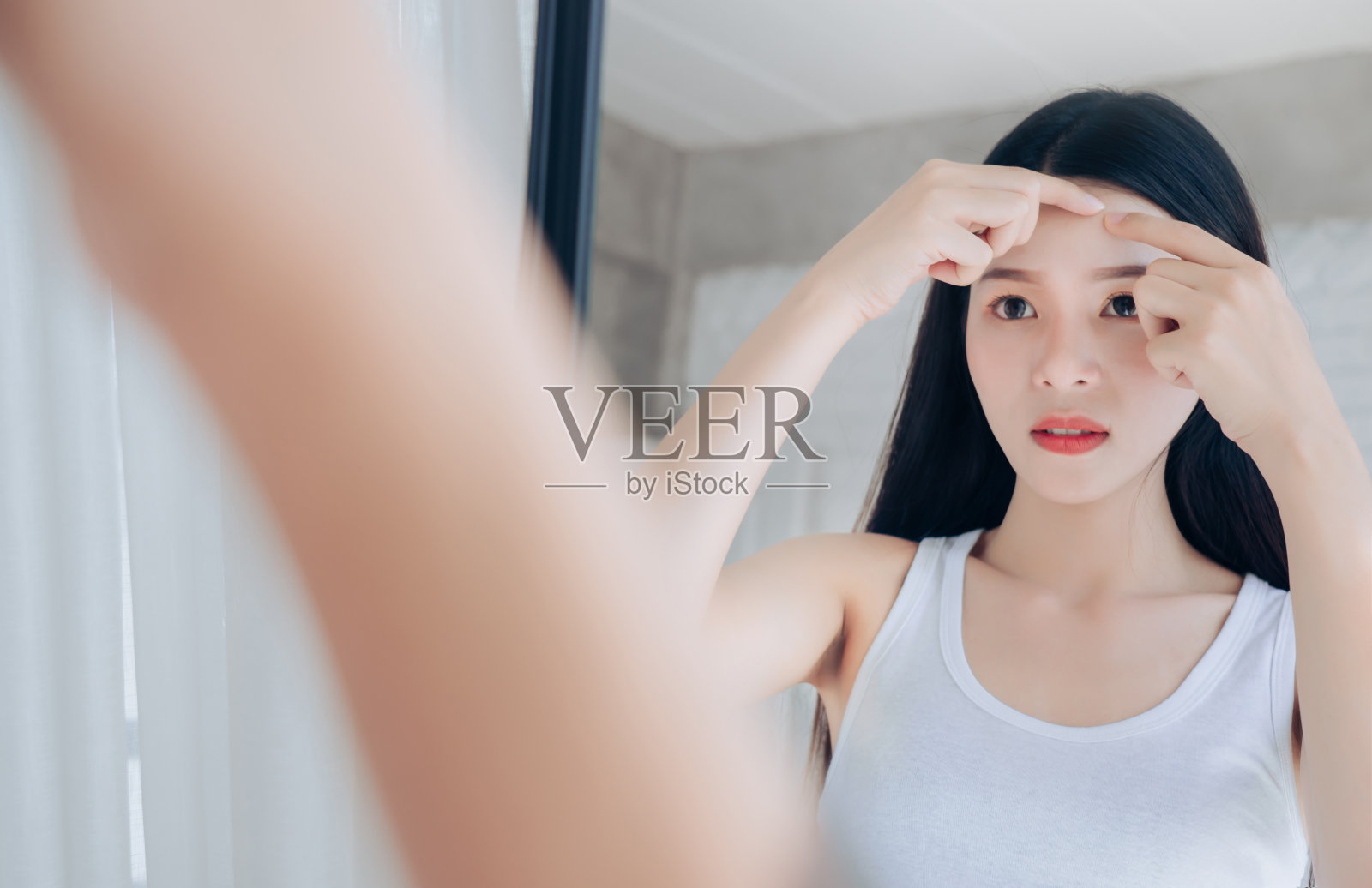 亚洲年轻女子在照镜子时脸上挤青春痘问题。照片摄影图片