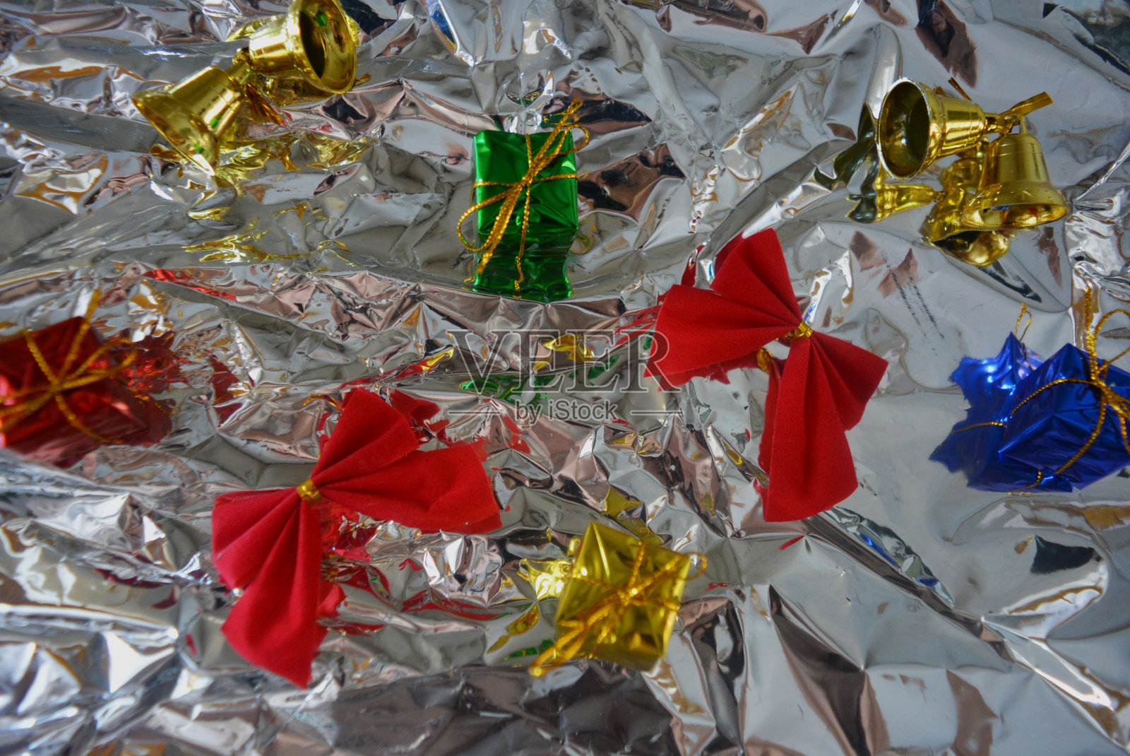 新年假期有红色的蝴蝶结和金色的铃铛，红色的蝴蝶结在光滑的铝，金属皱巴巴的纸上。照片摄影图片