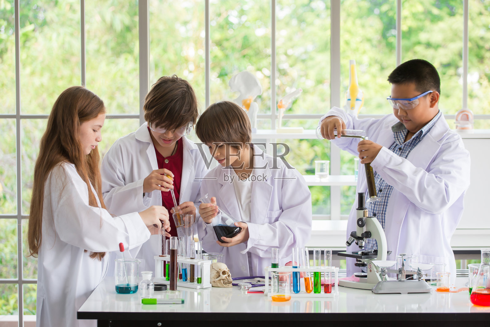 一群穿着白袍的学生在学校的实验室里做化学实验。在科学实验室里，孩子们用吸管将液体滴到试管中进行研究。多民族。亚洲人,白人,生物化学照片摄影图片