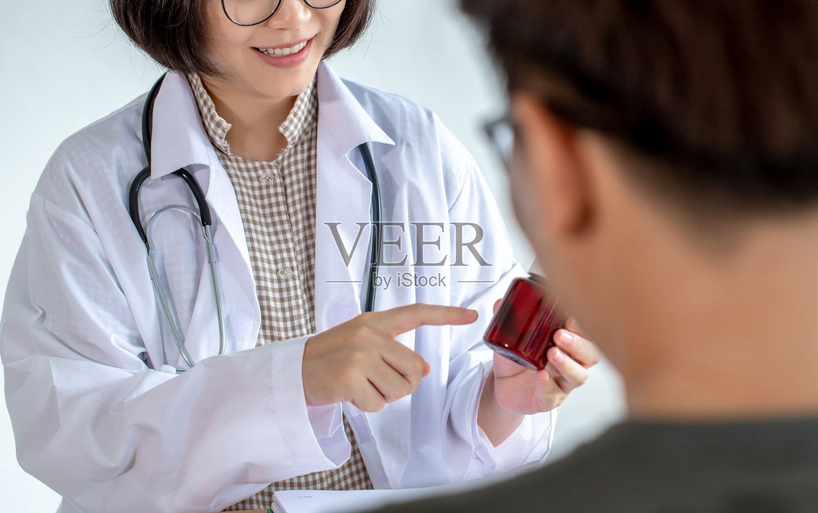 在诊所里，亚洲女医生向病人介绍药瓶。照片摄影图片