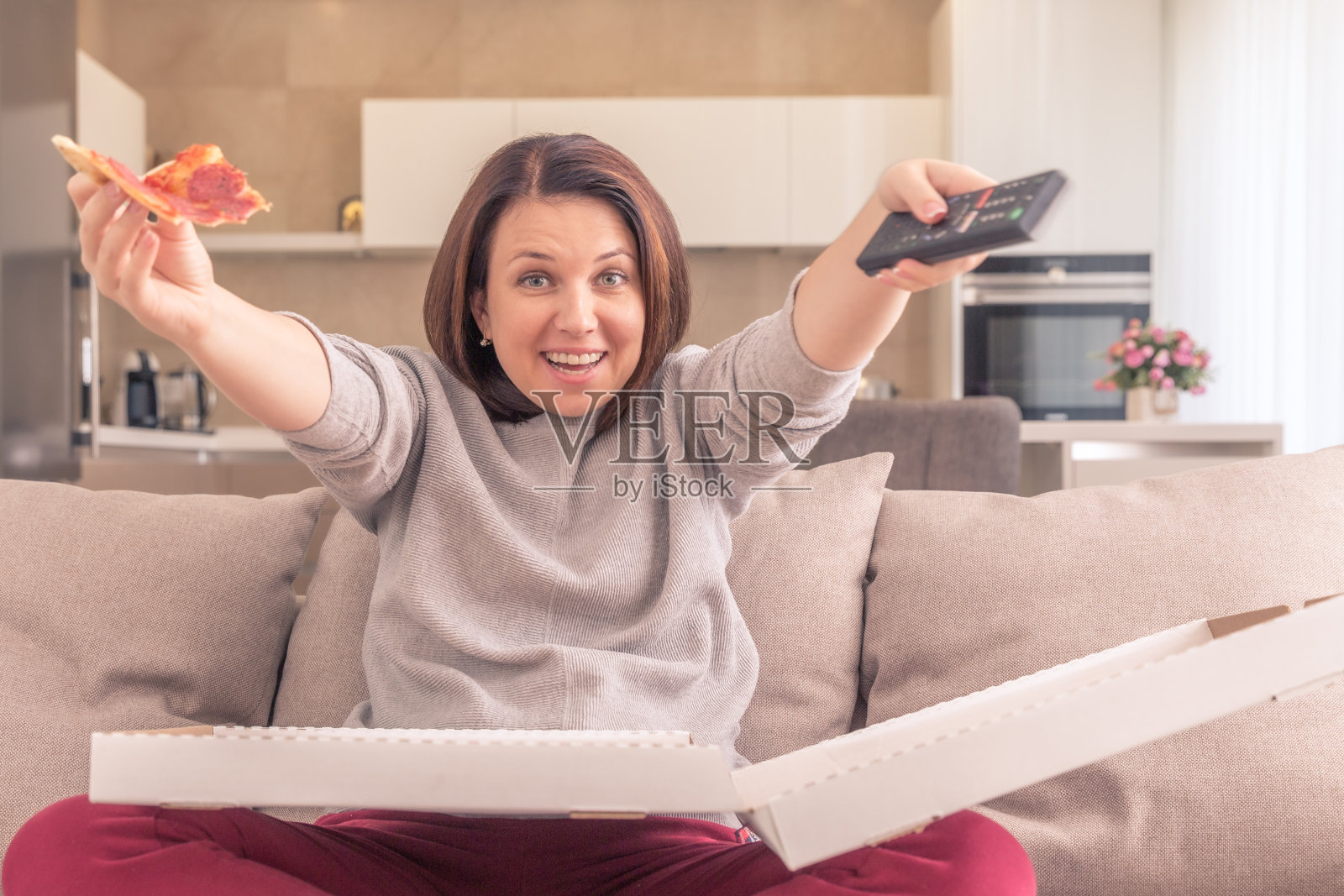 兴奋的女人在家里拿着遥控器边吃披萨边看电视，橙色调照片摄影图片