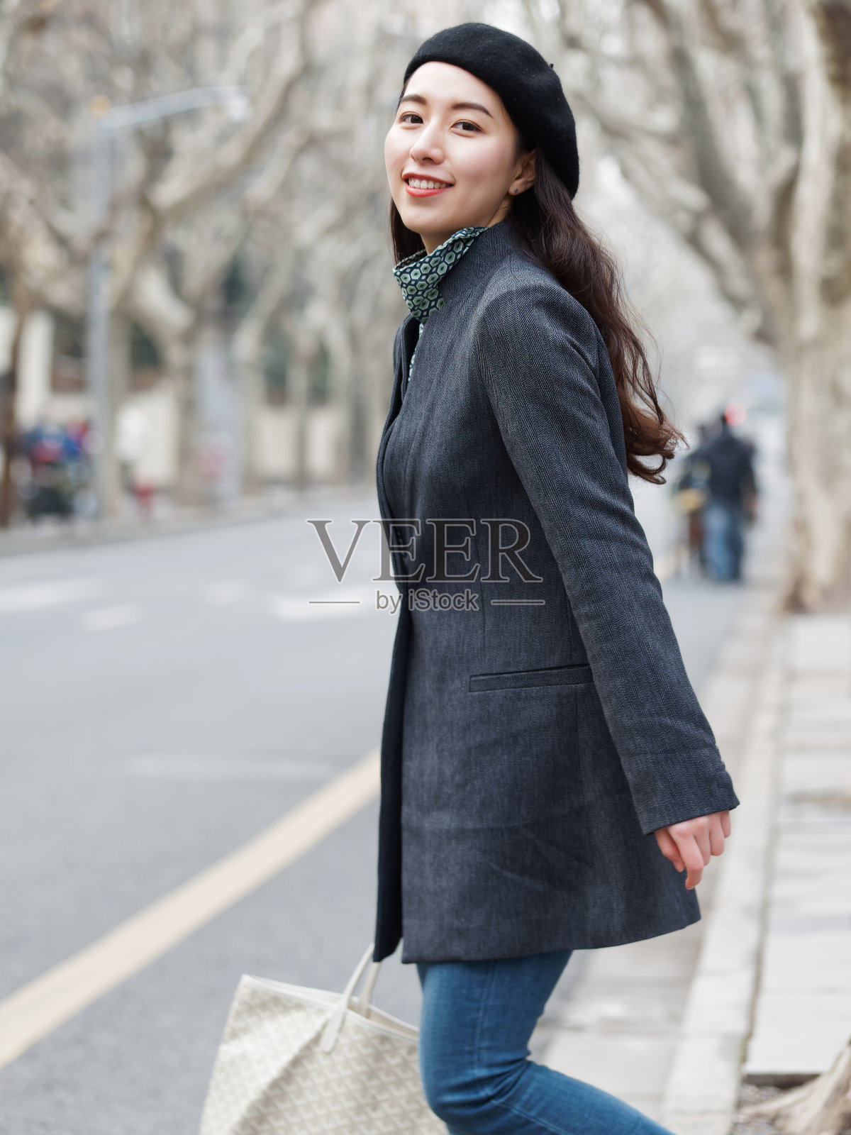 美丽的中国年轻女子在西装和牛仔裤走和过马路，微笑着在镜头与手拿包，自信的商业女性，户外时尚肖像魅力时尚女士。照片摄影图片