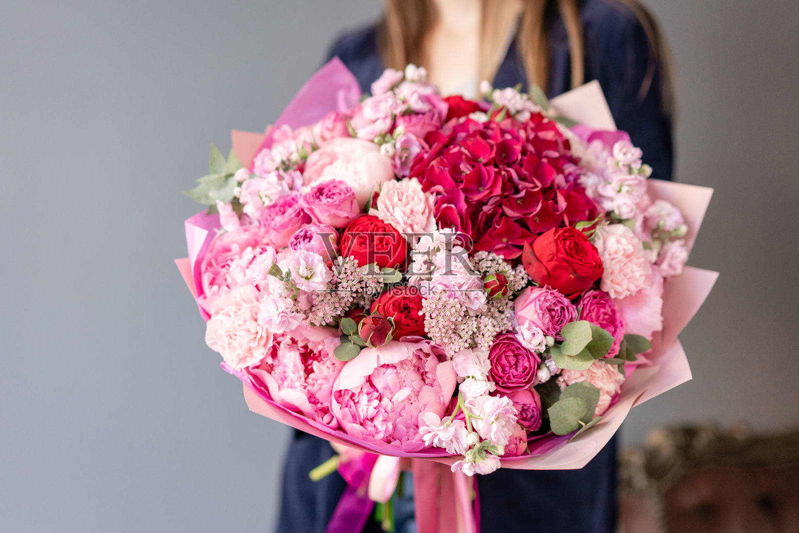 粉色的牡丹和红色的绣球花。女人手里拿着一束美丽的混合鲜花。花店概念。英俊的新鲜的花束。花交付。红色和粉红色。照片摄影图片