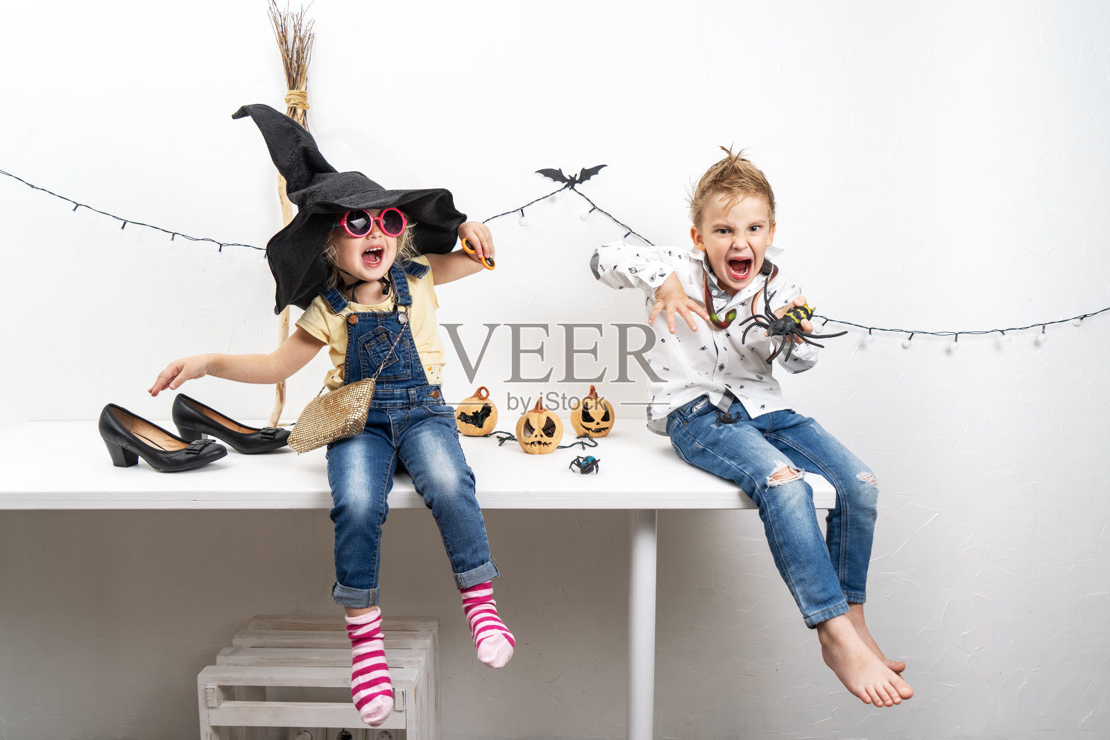 一个穿着僵尸服装的小男孩和一个穿着女巫服装的女孩正坐在桌子上。照片摄影图片