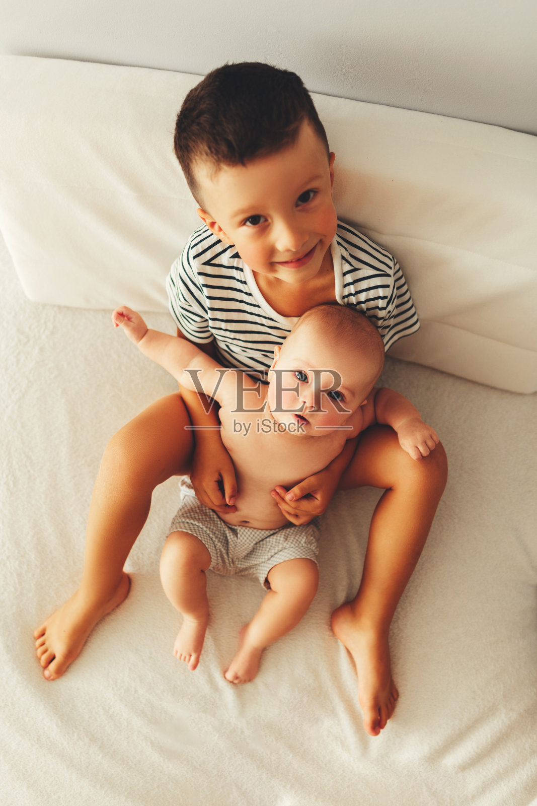 漂亮的婴儿和他的哥哥躺在床上。那孩子吻了他的小妹妹。照片摄影图片