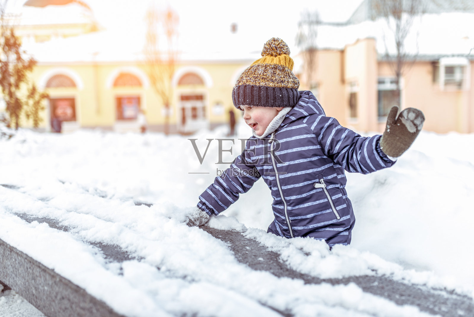 小男孩3-5岁，冬天在街上玩雪，穿着暖和的帽子蓝色工作服，背景是雪堆的雪。情绪，放松，周末。文本的空闲空间。照片摄影图片