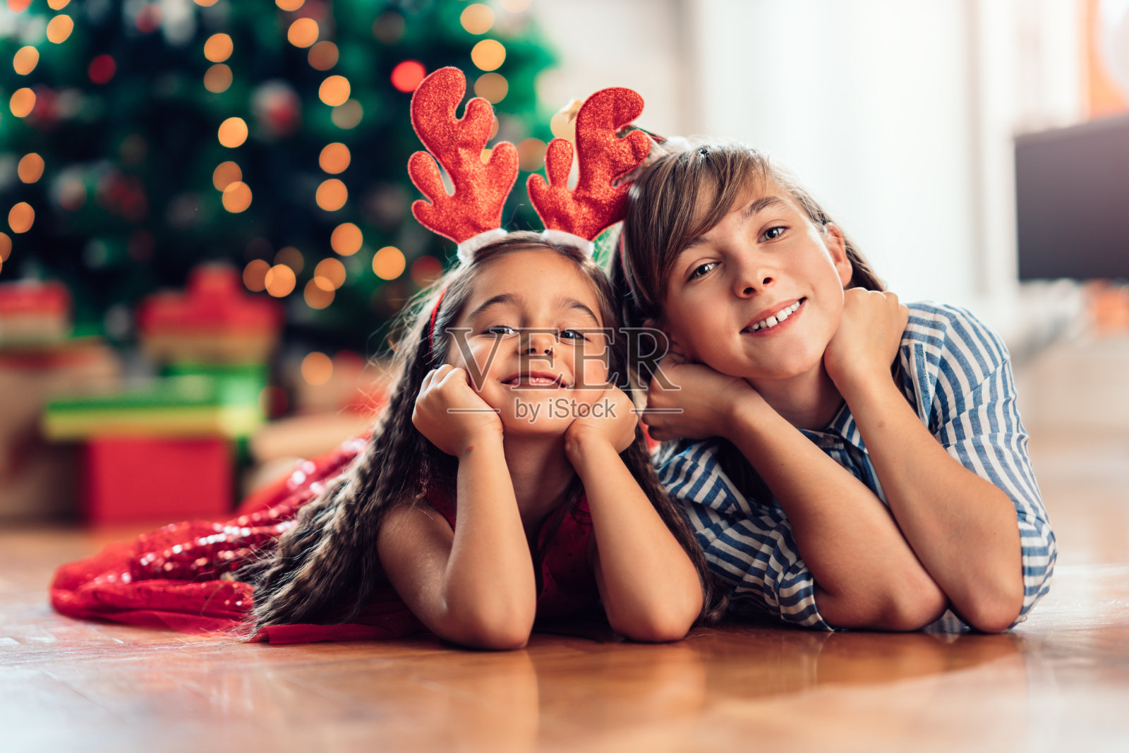 两个女孩躺在圣诞树前，戴着驯鹿的鹿角照片摄影图片