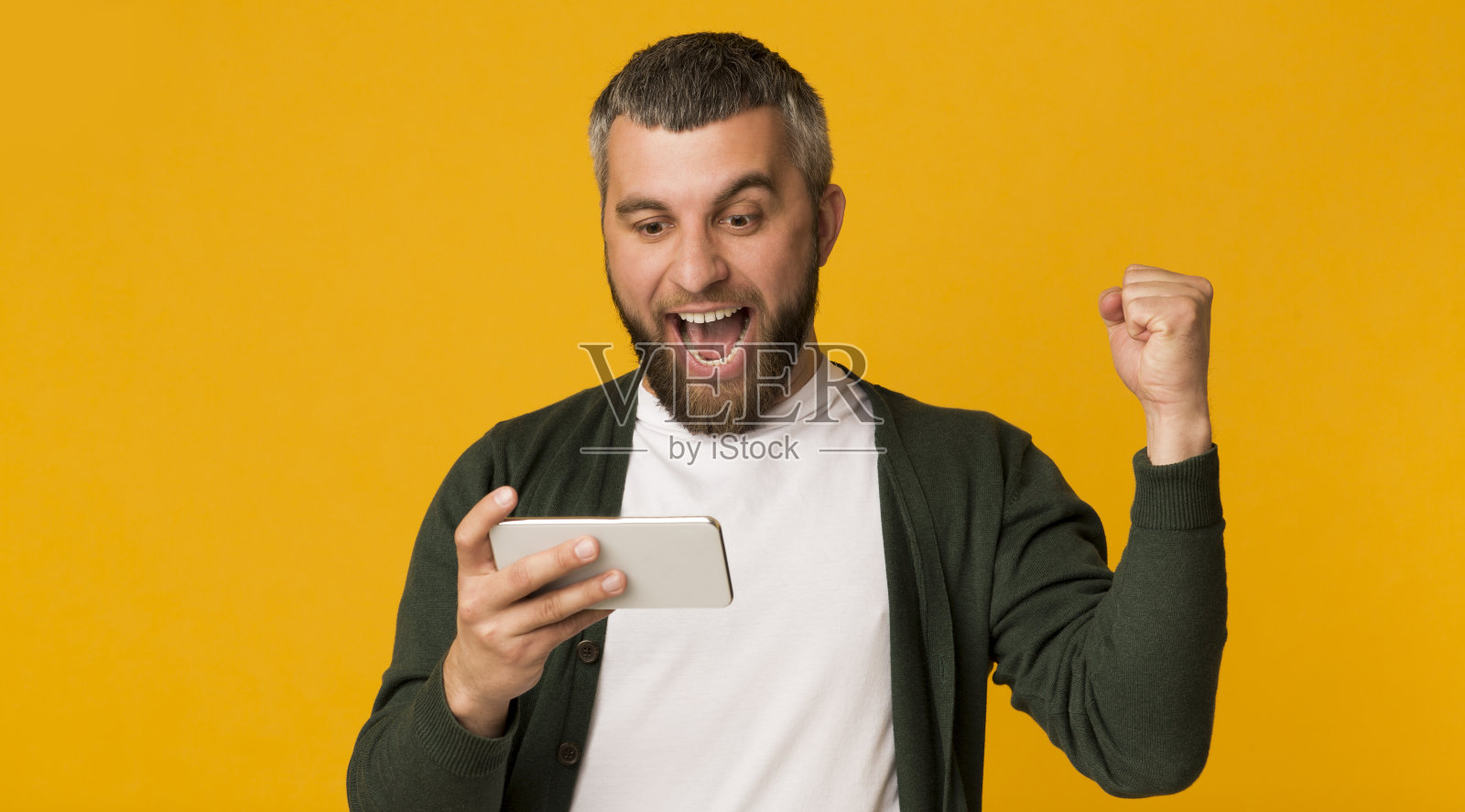 情绪激动的大胡子男人拿着智能手机，握紧拳头照片摄影图片