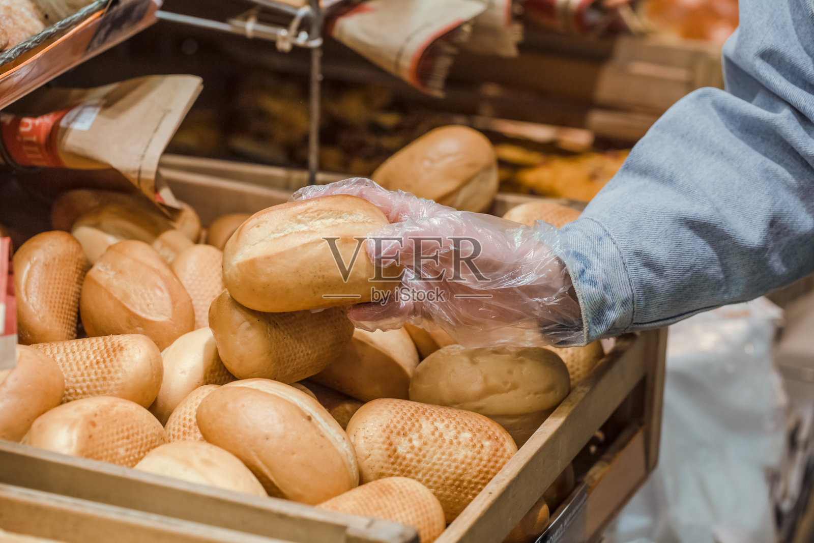 一位年轻的女士从超市的柜台上拿新鲜的面包。照片摄影图片