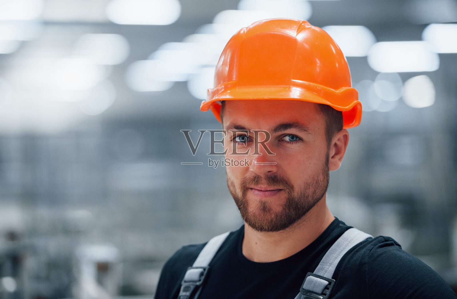 男性工业工人在工厂室内的肖像。戴着橙色安全帽的年轻技术员照片摄影图片