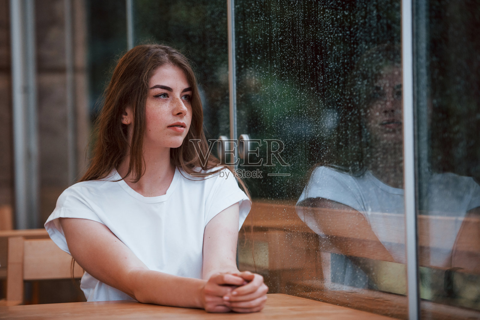 下雨天坐在咖啡馆里的年轻女孩的肖像。一个人只有照片摄影图片