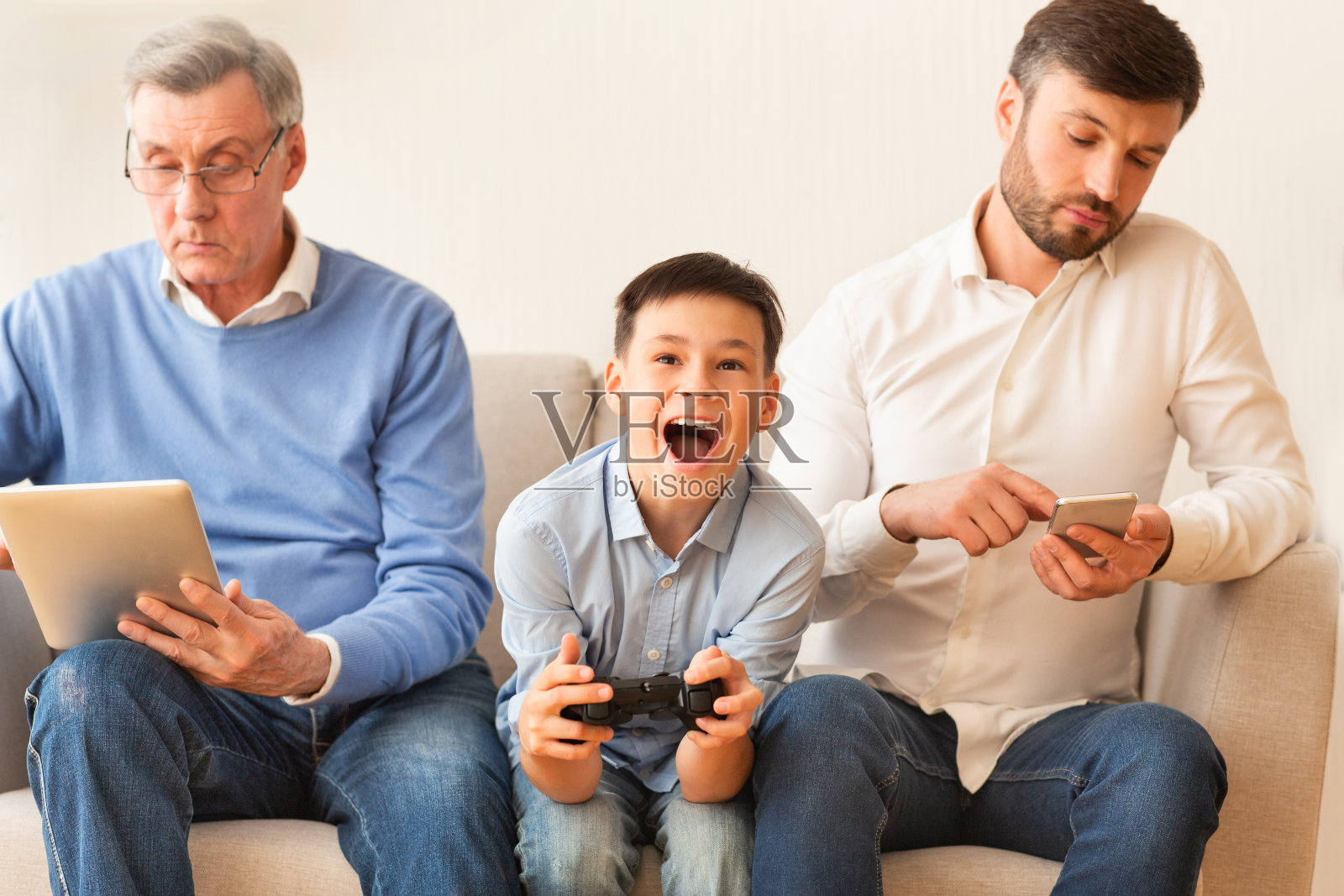 坐在爷爷和爸爸中间玩电子游戏的男孩照片摄影图片