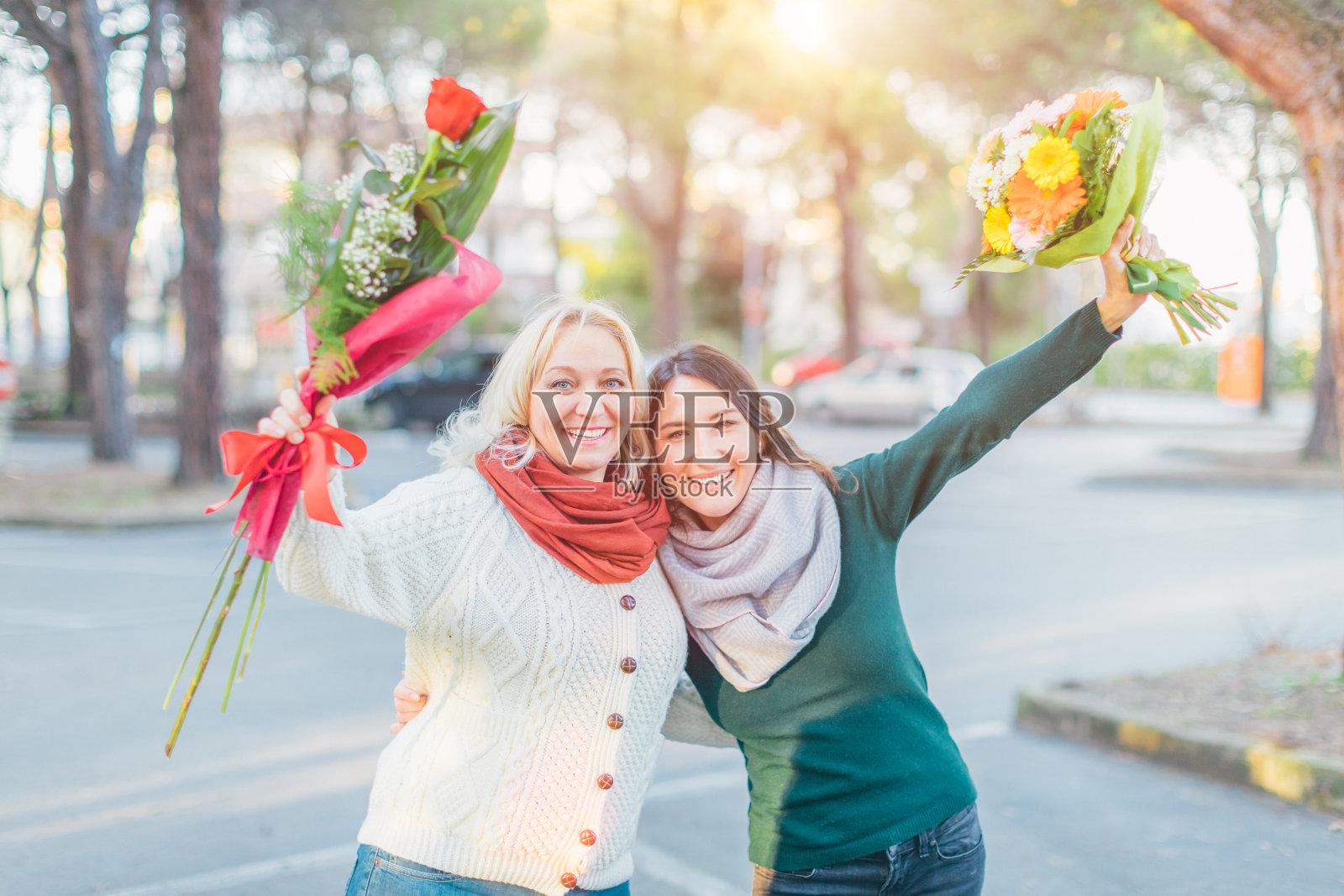 两个快乐的女人手里拿着鲜花，微笑着看着镜头——母亲和女儿在一起玩——春天和妇女节庆祝概念照片摄影图片