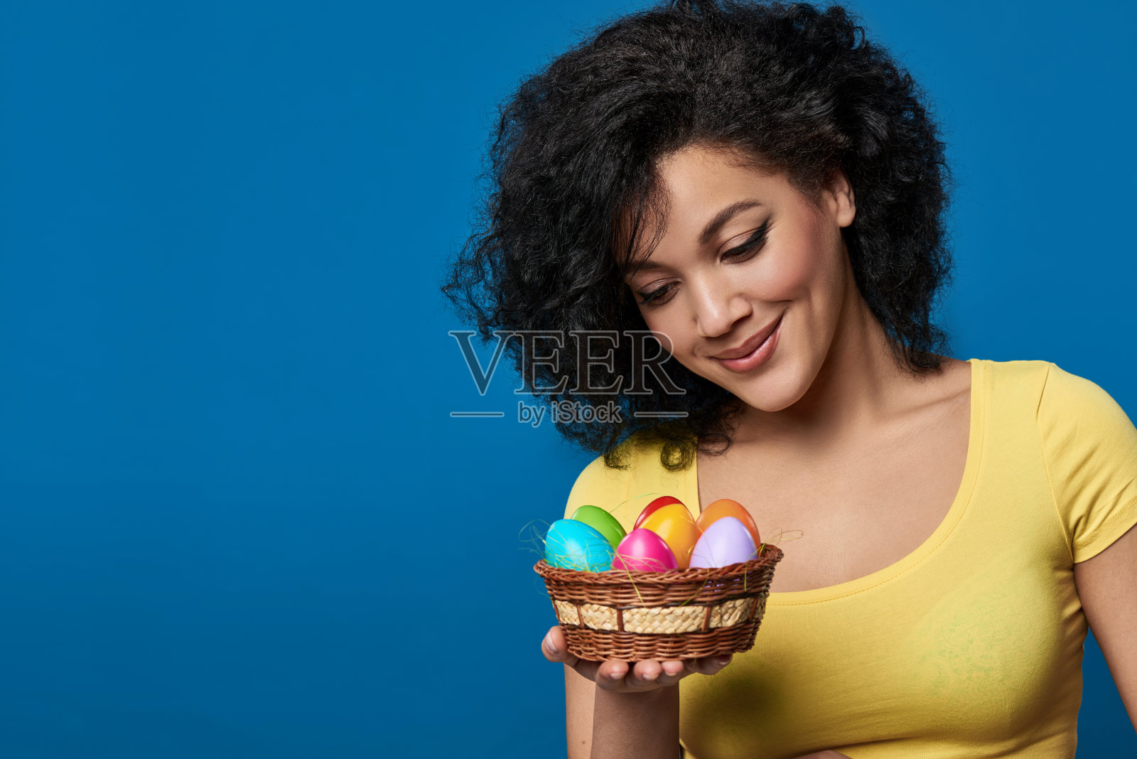 微笑的女人拿着一个篮子，里面有五颜六色的复活节彩蛋照片摄影图片