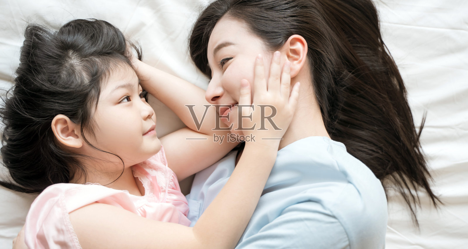 母亲和女儿在卧室里共度时光看着对方微笑。幸福的亚洲家庭照片摄影图片