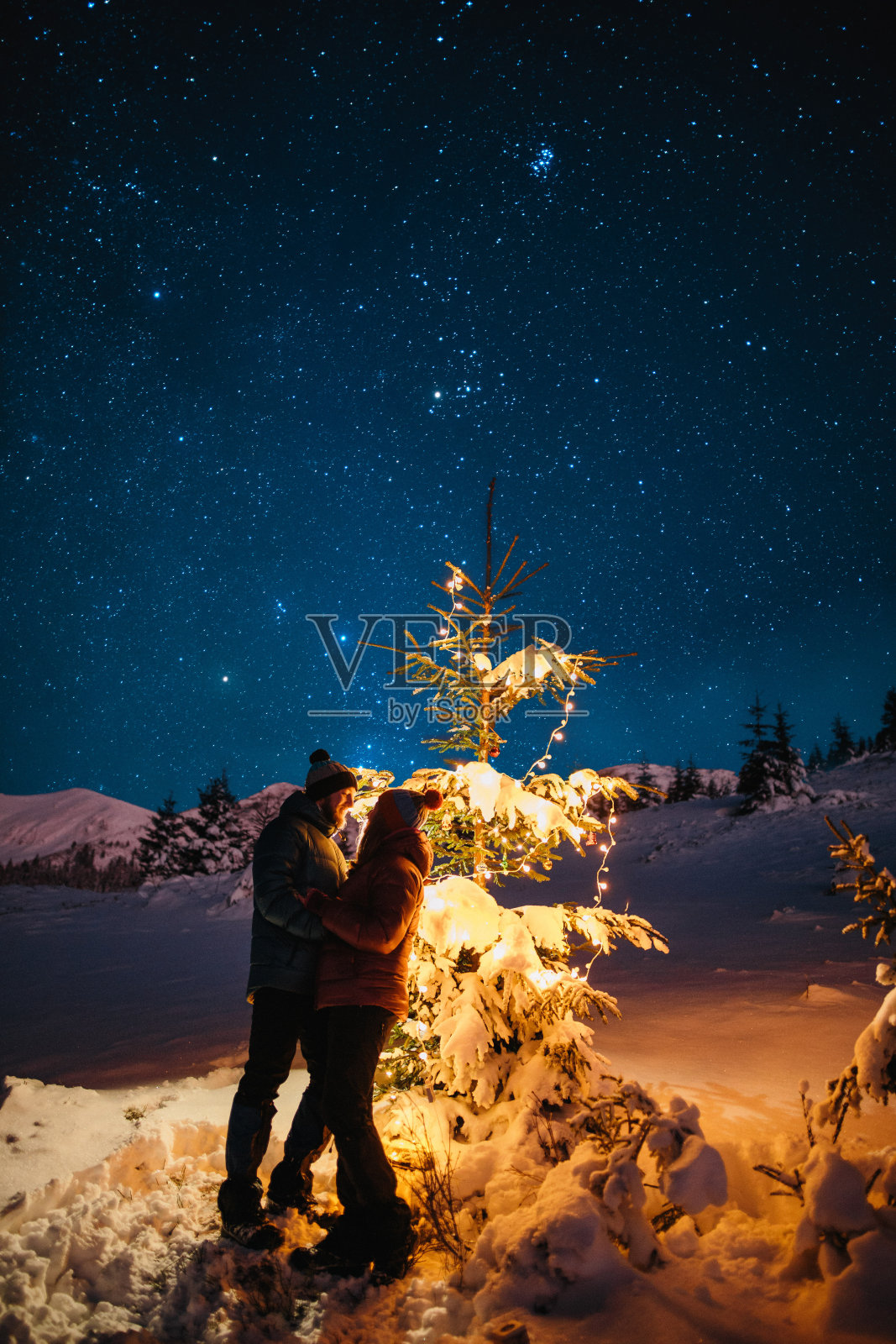 在冬天的星空下，一对情侣在明亮的圣诞树旁拥抱照片摄影图片
