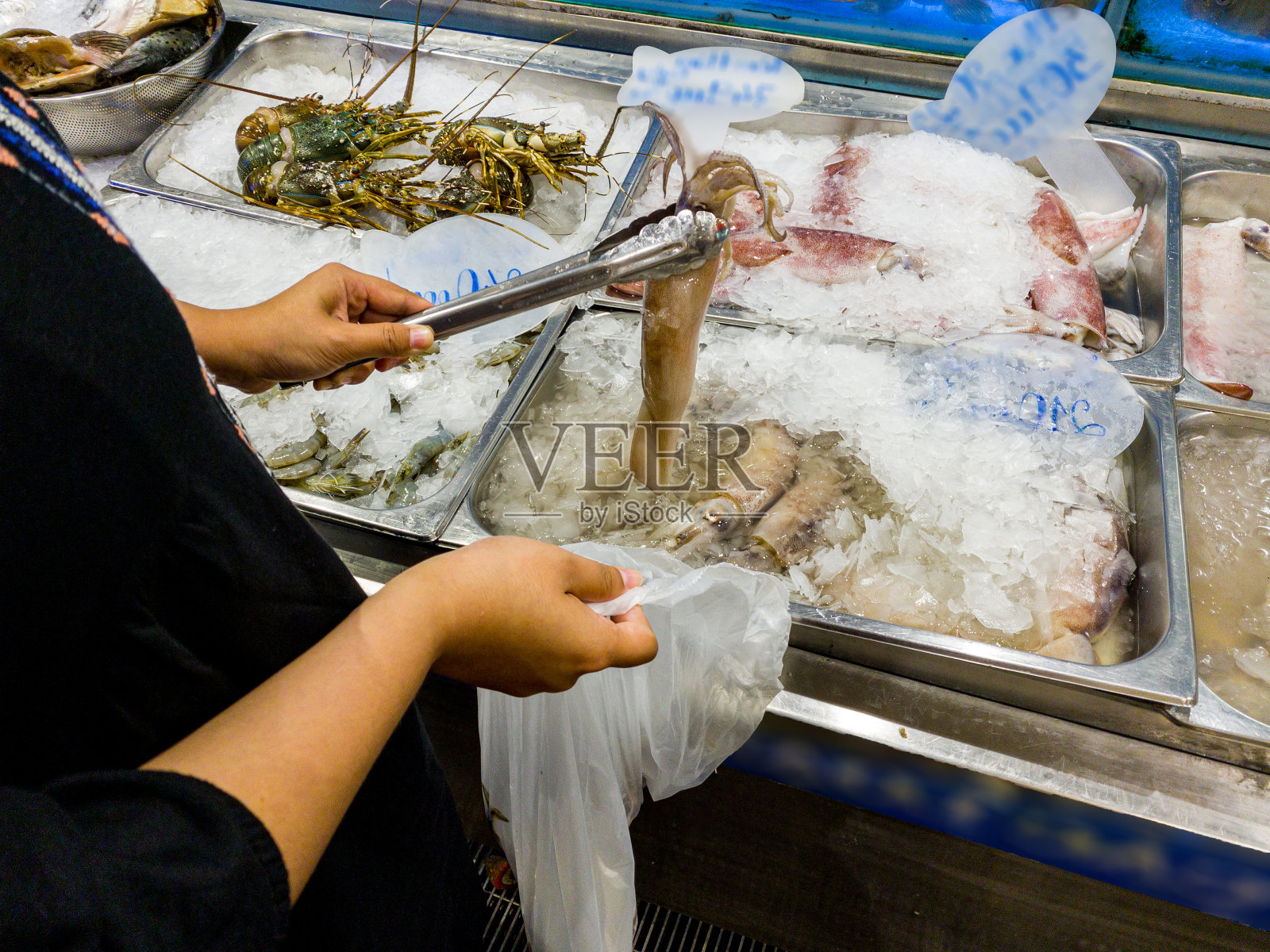 在海鲜超市挑选冷冻鱿鱼的女人照片摄影图片