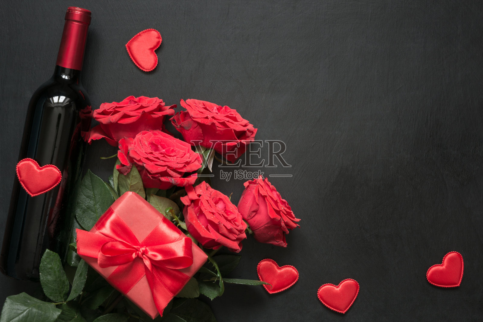 一束红玫瑰，一份礼物，黑桌上一瓶红酒。顶视图与空间。照片摄影图片