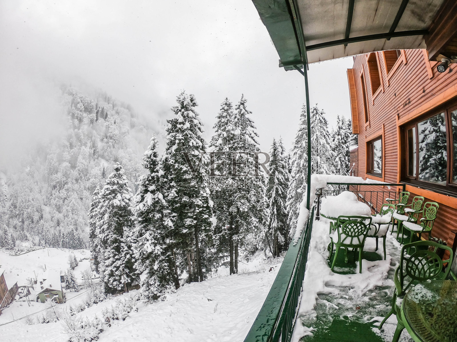 酒店阳台上的绿色桌子和椅子，雪花飘落在艾德的松树上照片摄影图片