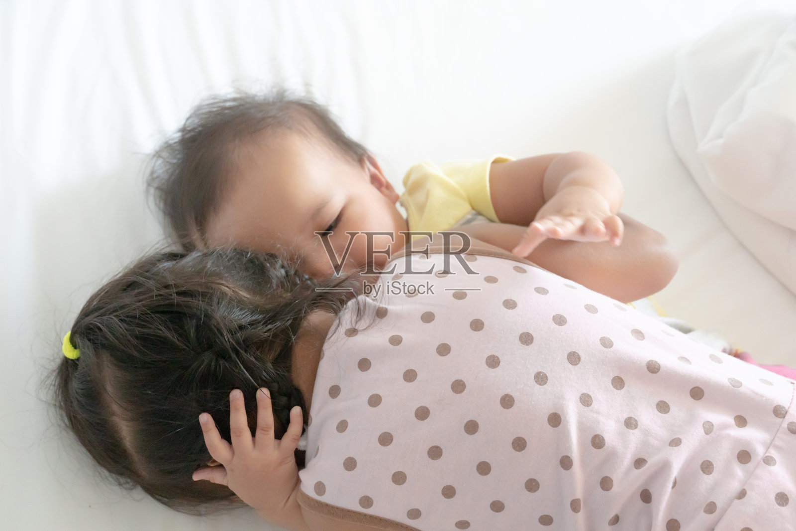 早上醒来后，两姐妹在白色的床上拥抱和翻滚。姐妹们互相表达爱意。照片摄影图片