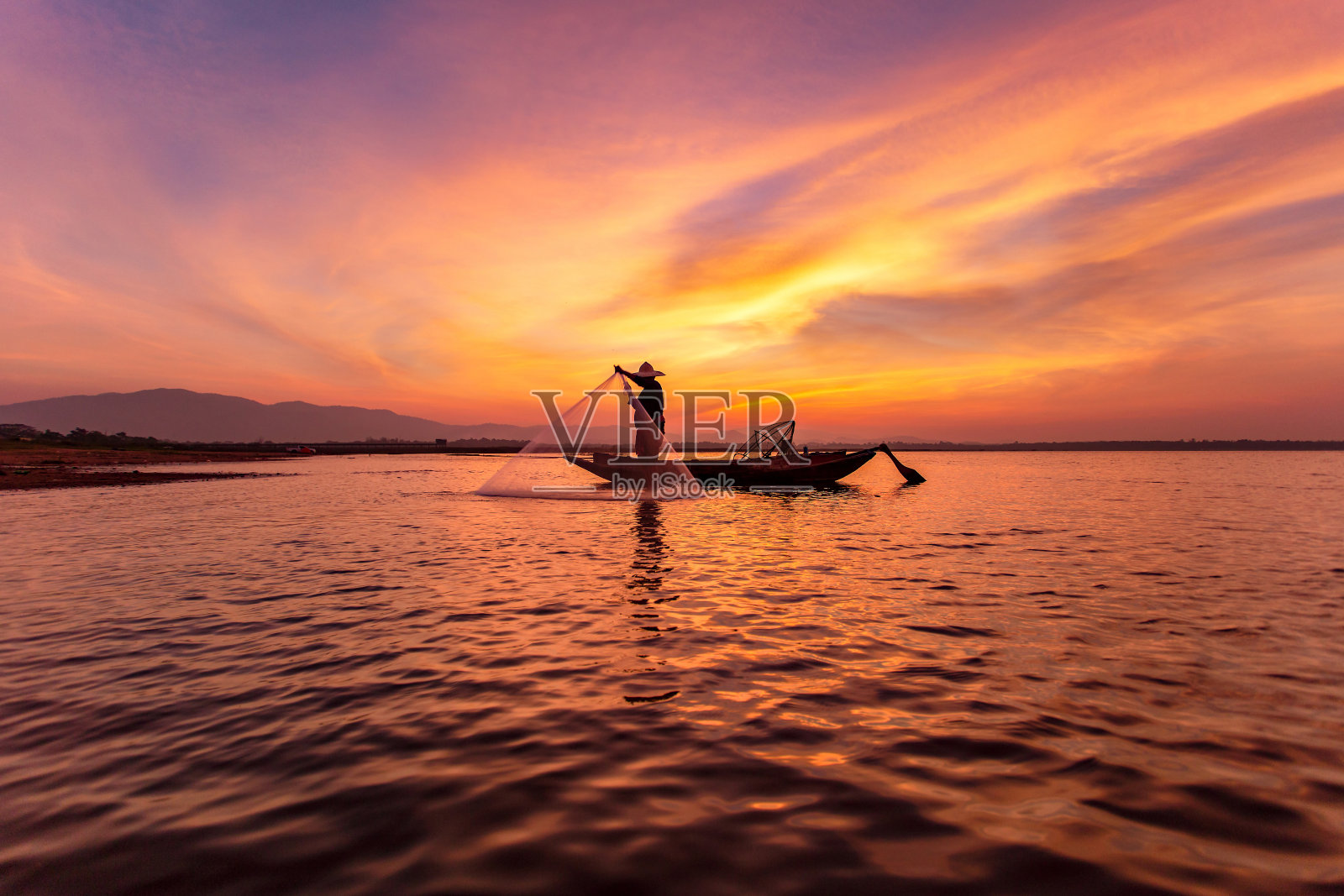 在美丽的日落背景下，渔民在湖上的船的剪影照片摄影图片
