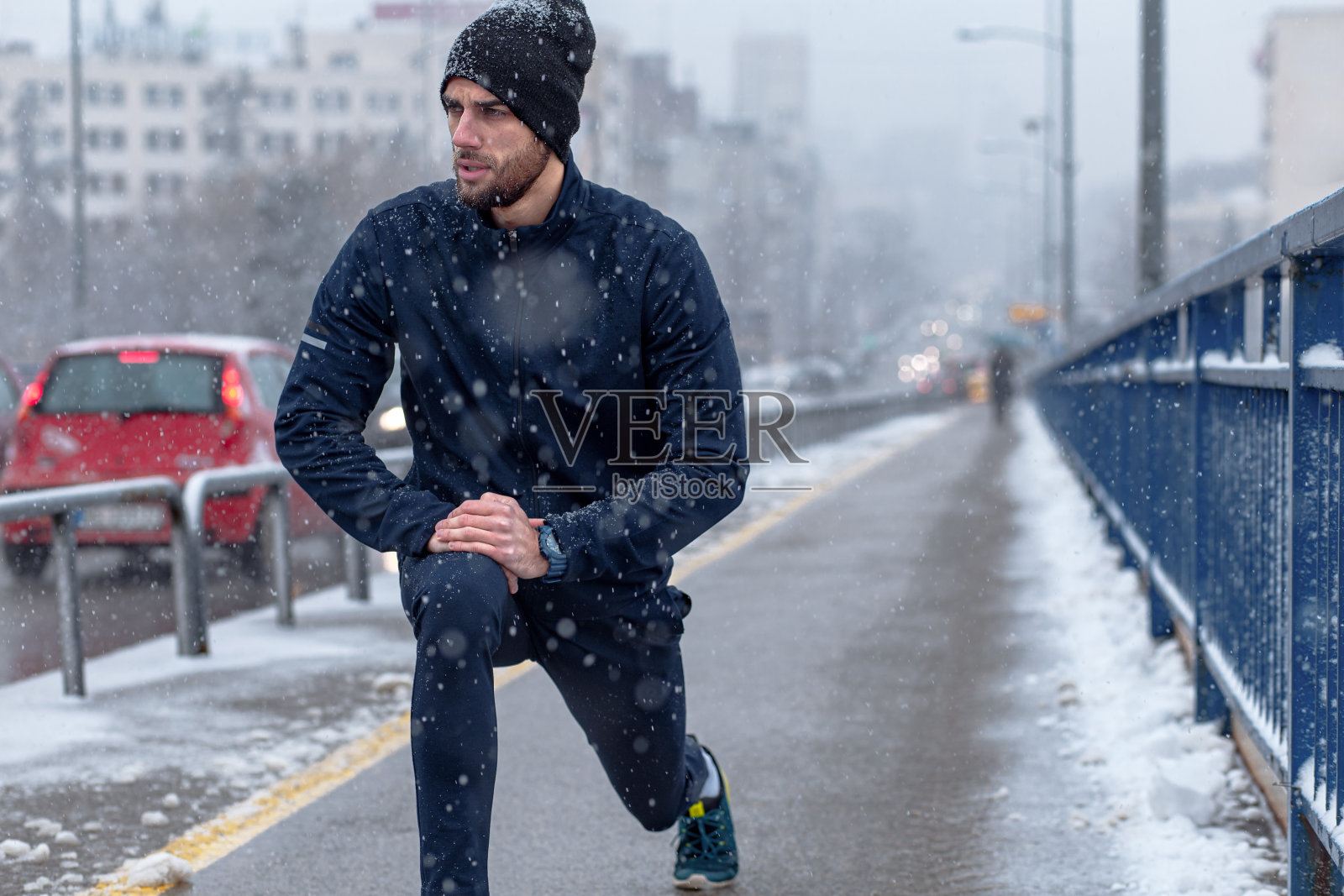 寒冷冬日的城市街道上，一名年轻人在跑步前伸了伸懒腰。照片摄影图片