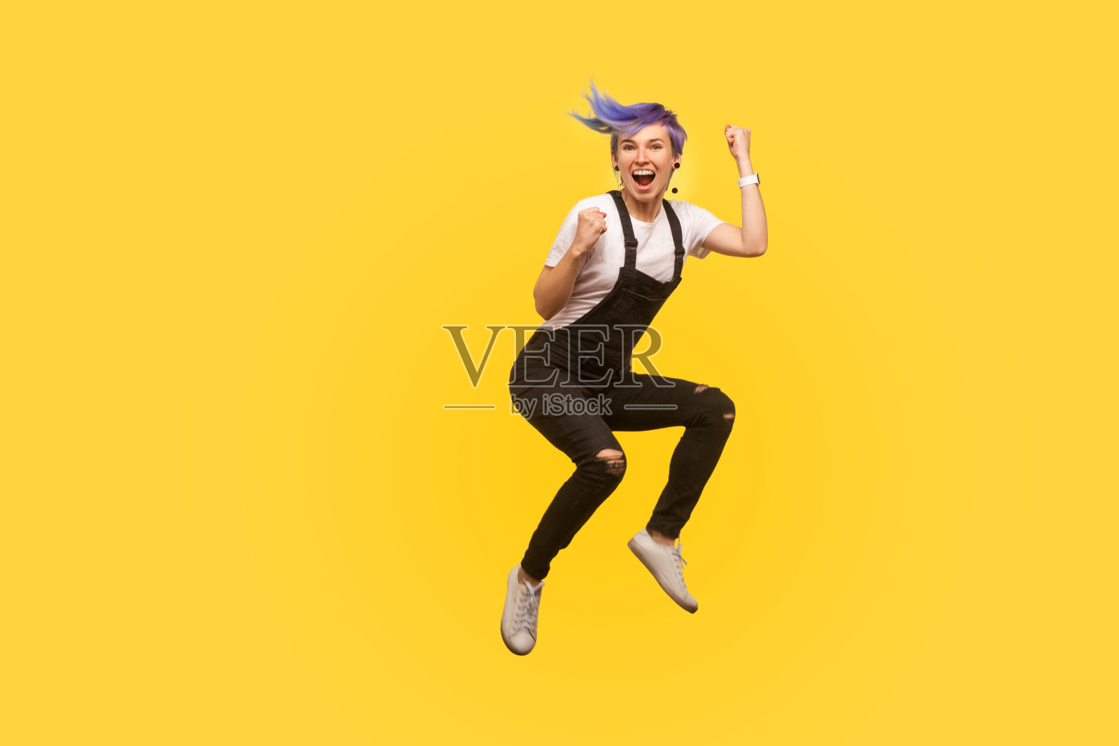 是的，我做到了!热情活泼的嬉皮女孩的肖像与紫色的头发在工作服跳在空中。黄色背景，工作室拍摄照片摄影图片