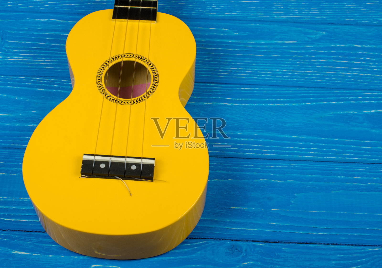 明亮的黄色尤克里里吉他的主体与明亮的蓝色木制背景照片摄影图片