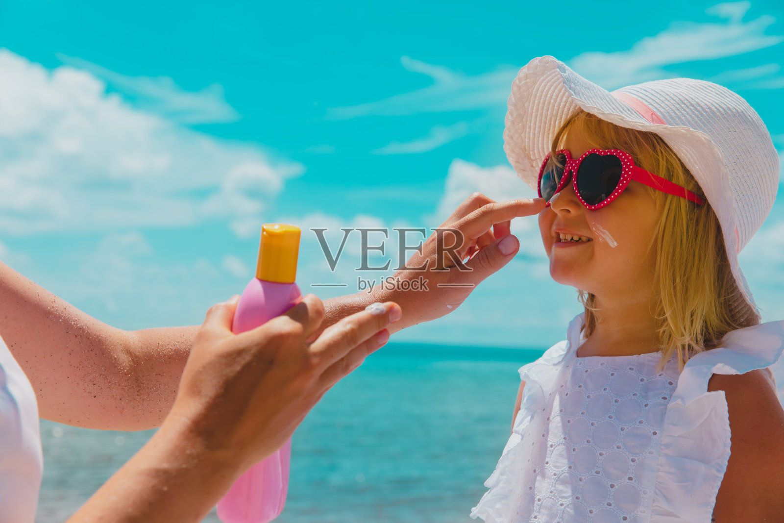 防晒——妈妈在海滩上给小女孩脸上涂防晒霜照片摄影图片