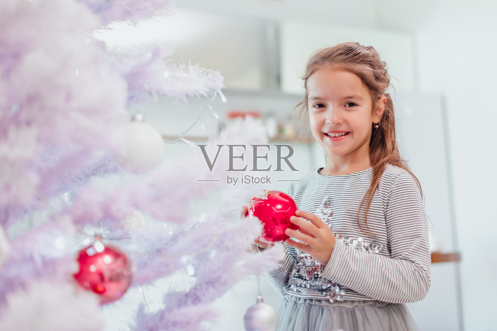 小女孩完全被圣诞树上装饰的彩灯和球迷住了。照片摄影图片