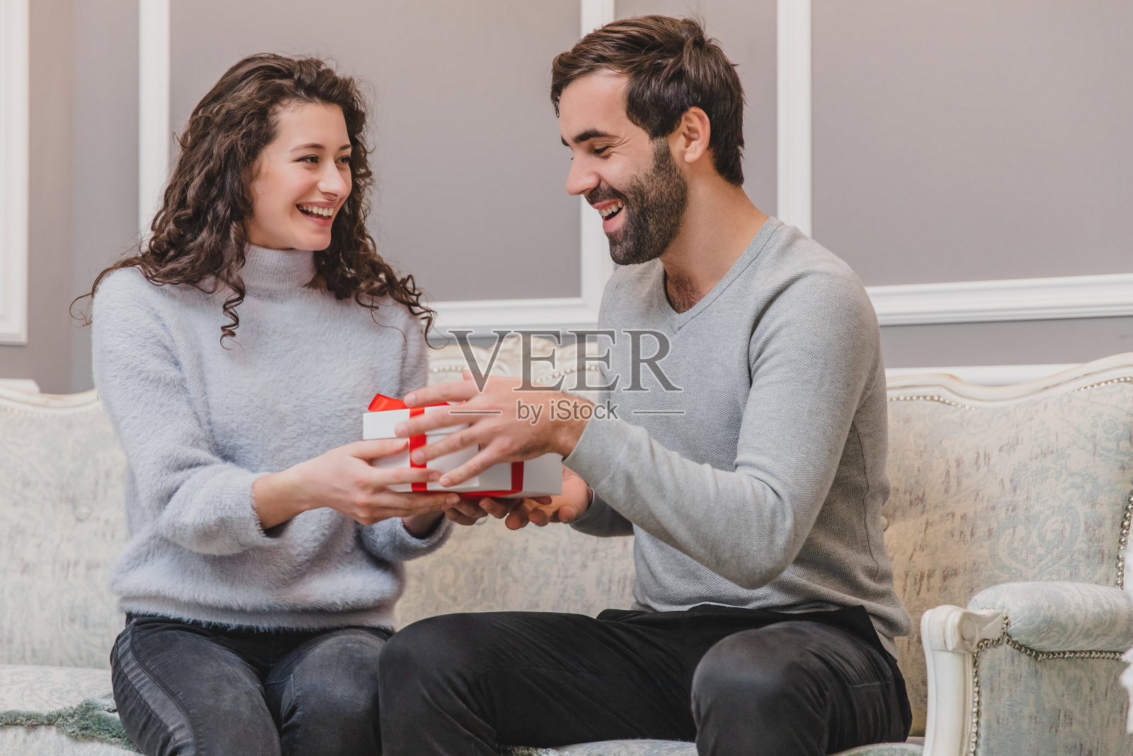 新年的时候，深情的小伙子坐在沙发上给女朋友送礼物。照片摄影图片