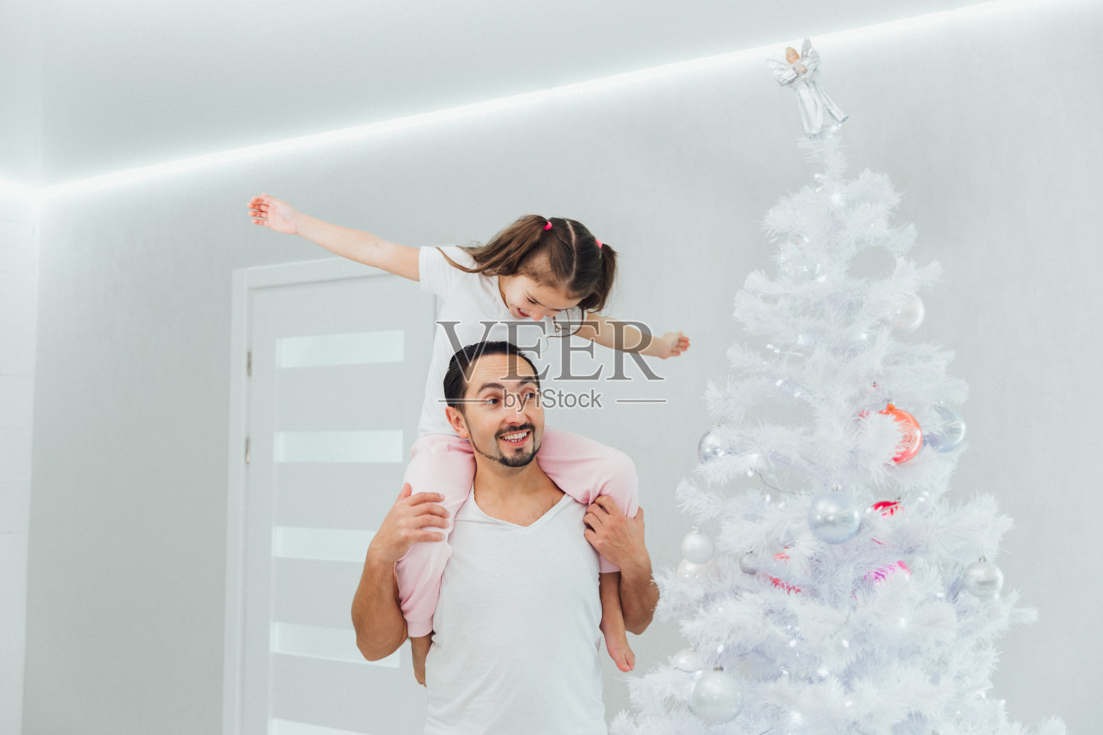 圣诞节。家庭。乐趣。爸爸和他的小女儿在家里的圣诞树旁玩耍照片摄影图片
