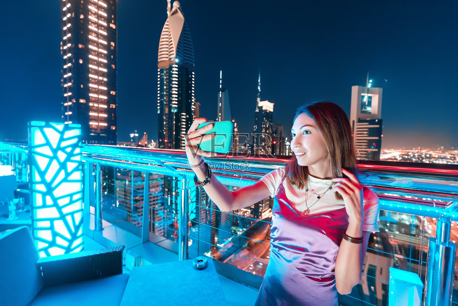 一名女博主在屋顶酒吧拍摄一张以摩天大楼为背景的夜城自拍照片摄影图片