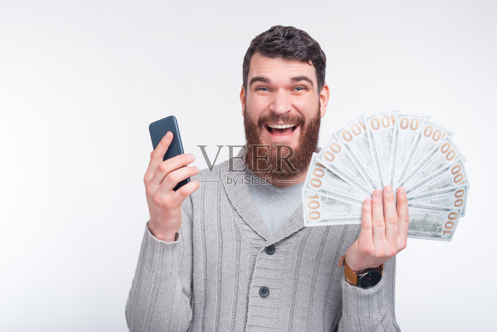 看看我在博彩网站上赢了多少钱。一个激动的大胡子男人在镜头前展示着他的手机和一些钱。照片摄影图片