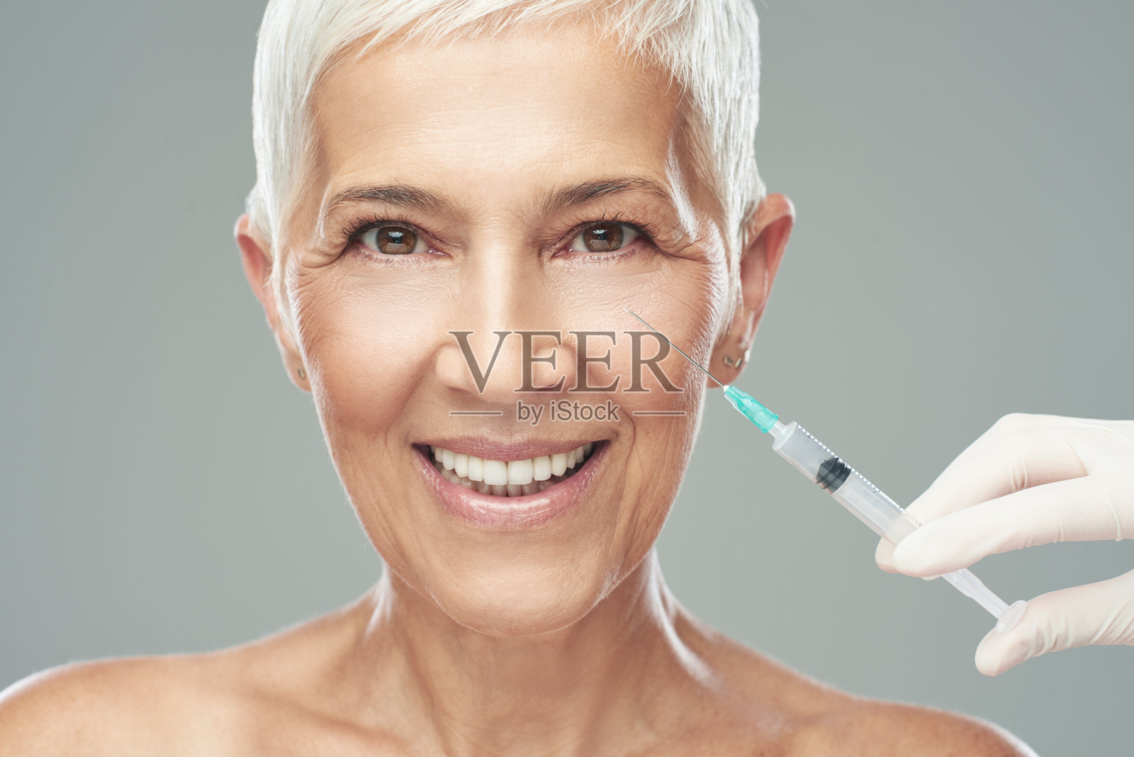 美丽微笑的白人老年妇女站在灰色的背景和拍摄抗衰老产品。美摄影。照片摄影图片