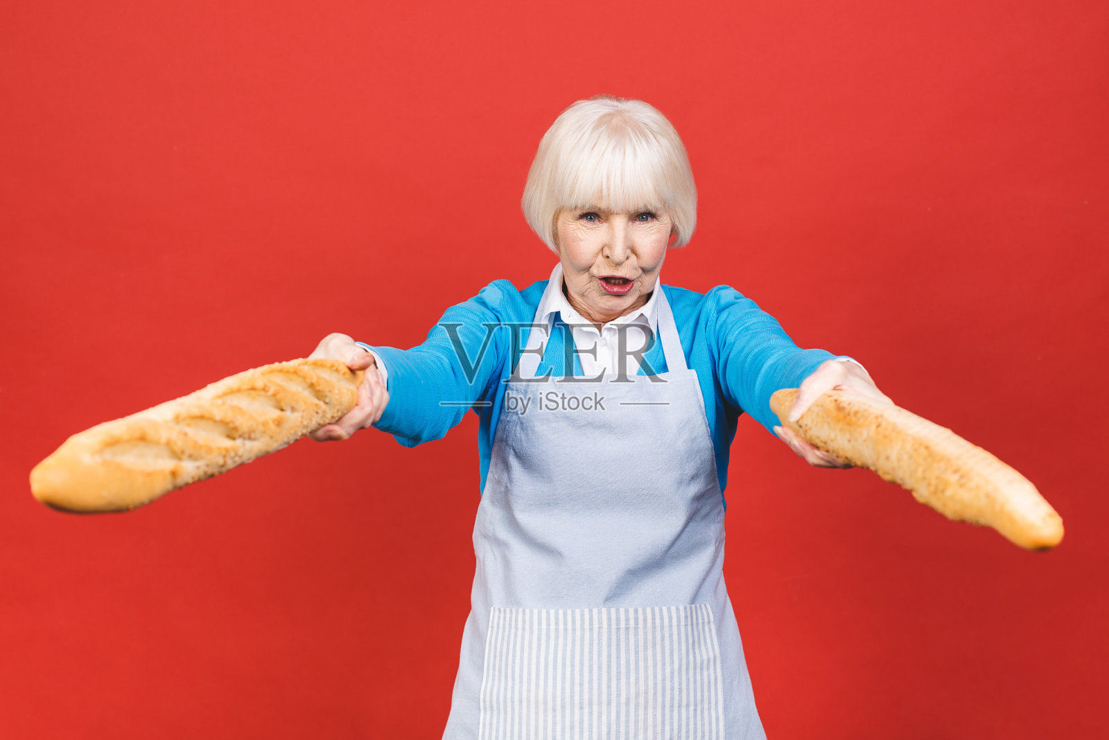 法国的味道。一个快乐的妇女的肖像拿着一个新鲜美味的法棍面包微笑孤立在红色的背景。面包店的概念。照片摄影图片