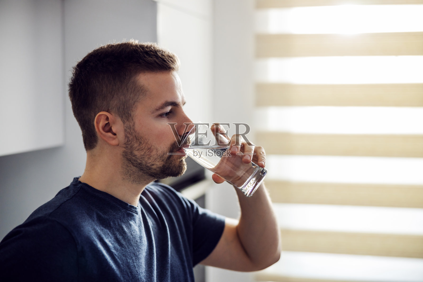 侧面的英俊的口渴的男子喝淡水。家庭内部。照片摄影图片