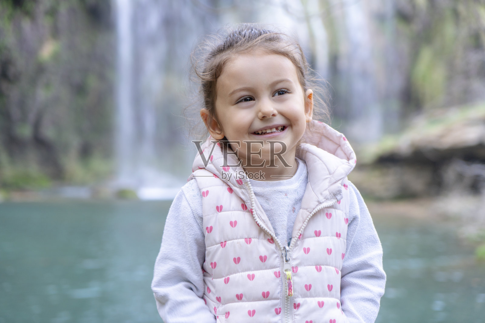 微笑的小女孩在瀑布旁的肖像照片摄影图片