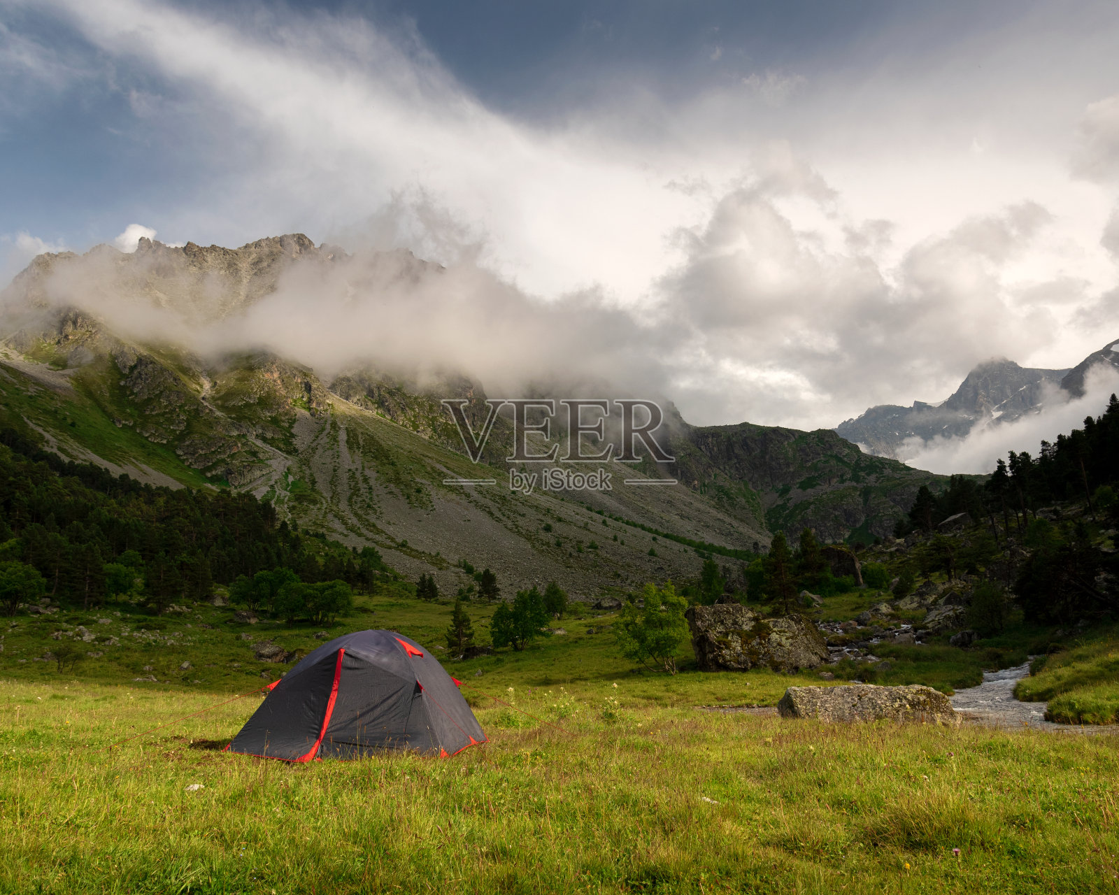 旅游帐篷伫立在一片绿油油的草地上，背景是山坡和山峰照片摄影图片