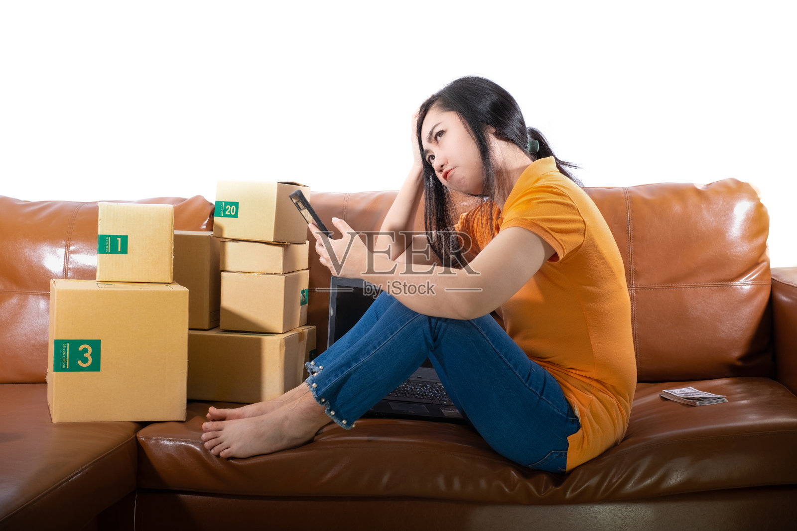 一个无聊的年轻女人正坐在她房间的沙发上，女人用手机在白色的背景上，一个女士是无聊的，因为销售额从销售目标概念下降照片摄影图片