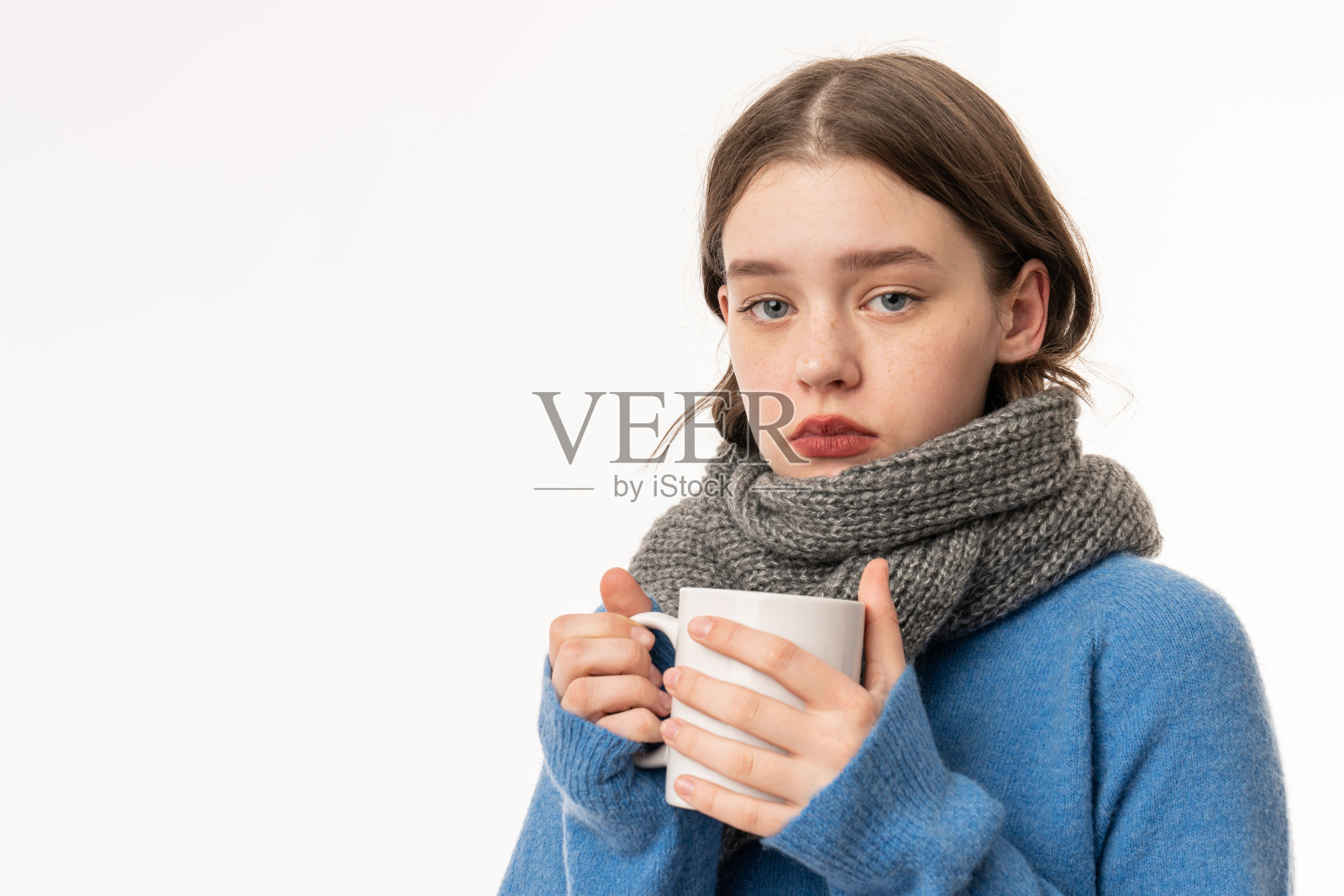 一个沮丧的女孩的肖像穿着毛衣和围巾孤立在白色的背景，拿着一杯热茶照片摄影图片